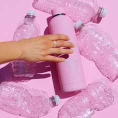 a woman's hand holding a pink water bottle surrounded by plastic bottles