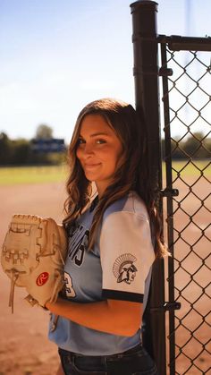 a woman holding a catchers mitt next to a chain link fence at a baseball field