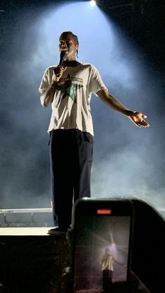 a man standing on top of a stage with his arms out to the side while holding a microphone