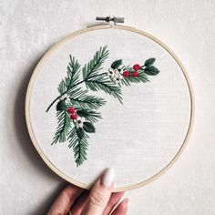 someone is holding up a cross - stitch christmas ornament with holly and berries on it