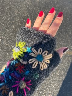 a woman's hand with red fingernails holding up a gray knitted mitt covered in multicolored flowers