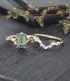 a ring with an emerald colored stone surrounded by small white diamonds on a wooden surface