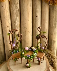 a wooden table with two chairs and flowers on it, in front of a wood fence