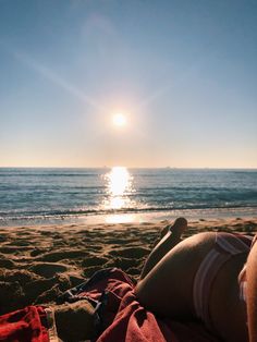 a woman laying on top of a sandy beach next to the ocean under a bright sun