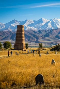 an old tower in the middle of a field with mountains in the background and text explaining exploring krygyzstan's burma tower