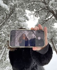 a woman taking a selfie with her cell phone in the winter snow covered forest