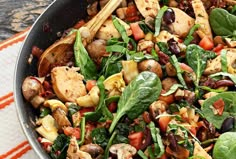 a skillet filled with spinach, chicken and other vegetables on top of a table