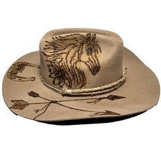 Cowboy hat custom burned by hand specifically for Bourbon Cowgirlby KC Lids. These hats are exclusive and only found here. We worked with the designer to create our very own look. 100% wool hat. One size fits all, as the interior band is adjustable to fit most. A beautiful cattleman rancher style, this distressed almond / beige colored hat is sanded and torched to a beautifully burnished and distressed finish. Firm shape (do not crush). Our artisan has hand burned a beautiful horse with flowing Artisan Curved Brim Hat For Western-themed Events, Luxury Rustic Brimmed Cowboy Hat, Women’s Felt Cowboy Hat, Brimmed Hats For Western-themed Country Festivals, Luxury Country-style Cowboy Hat For Festivals, Horse Flowers, Country Music Concerts, Hand Burn, Bullet Shell