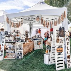 a group of people standing under a white tent with lots of items on display in front of it