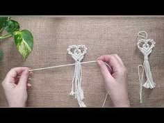 two hands are working on some white string with flowers in the middle and one hand is knitting