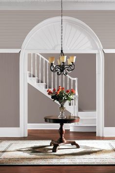 a dining room table with flowers on it in front of a staircase and chandelier