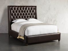 a bed with white linens and brown leather headboard, in a gray room