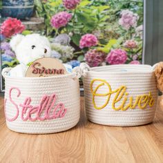 two white baskets with the word stella and a brown teddy bear sitting next to them