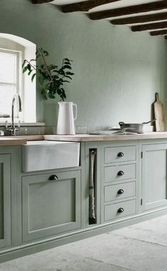 a kitchen with green cabinets and a white vase on the counter top, in front of a window