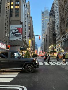 a busy city street with people crossing the street and cars driving on the road in front of tall buildings