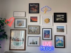 a wall filled with lots of framed pictures and neon signs next to a potted plant