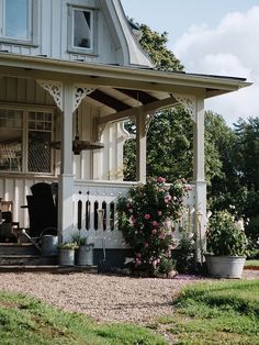 a white house with lots of flowers on the front porch and covered porch area next to it