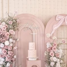 a pink wedding cake sitting on top of a table next to two wreaths with flowers