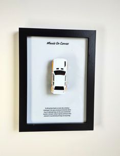 a white toy car in a black frame on the wall above it's display