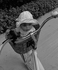 a baby in a white hat is riding a bike with a basket on the handlebars