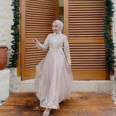 a woman standing in front of a wooden door wearing a white dress and head scarf