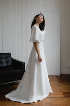 a woman in a white dress standing on a wooden floor with her arms behind her head