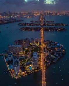 an aerial view of a city at night with lights on the buildings and water in the foreground