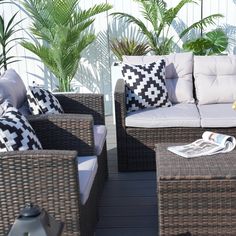 two wicker couches with pillows sit on a deck next to potted plants