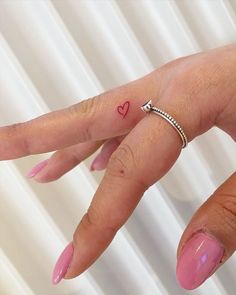 a woman's hand with a small red heart tattoo on her left ring finger