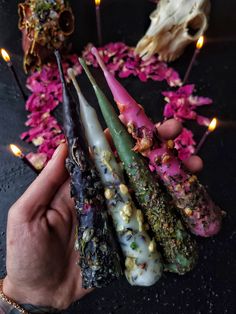 a person holding several different types of candles in front of some skulls and flowers on the ground