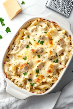 a casserole dish with chicken, cheese and parsley in it on a white table