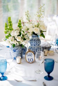 two blue and white vases with flowers in them on a table set for an event