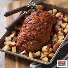 meat and potatoes in a pan on a wooden cutting board with two serving utensils