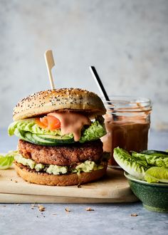 a hamburger with lettuce, tomato and cucumber on it next to a jar of dressing