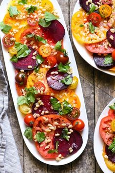 two white plates filled with different types of vegetables on top of a wooden table next to each other