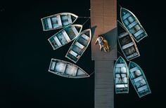 two people are standing on the dock next to several small canoes that have been tied together