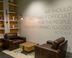 two leather chairs and a table in front of a wall with words on the wall