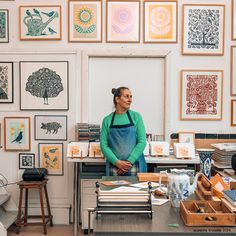 a woman standing in front of a desk with lots of art on the wall behind her