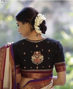 a woman wearing a black and white sari with flowers in her hair is looking down