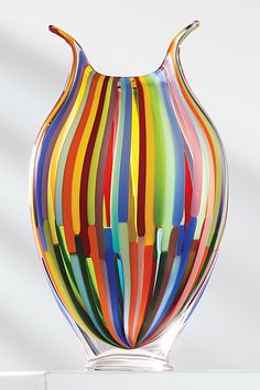 a multicolored glass vase sitting on top of a white table next to a wall