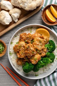 a white plate topped with chicken and broccoli on top of rice next to orange slices