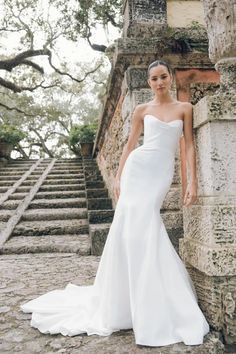 a woman standing in front of some stairs wearing a white wedding dress and headpiece