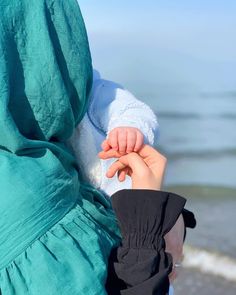 a young child holding onto an adult's hand on the beach with water in the background