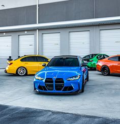 four different colored cars parked next to each other in front of two garage doors with roller doors