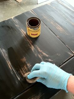 a person in blue gloves painting a wooden table with brown paint on top of it