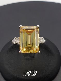 a fancy yellow diamond ring sitting on top of a black surface with diamonds around it