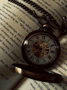 an old pocket watch sitting on top of an open book with chain attached to it