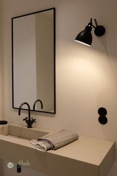 a bathroom sink under a mirror next to a wall mounted light and black faucet