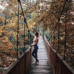 a woman standing on a wooden bridge in the woods