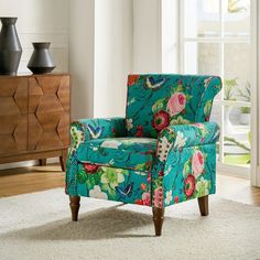 a blue chair with flowers on it sitting in front of a white rug and window